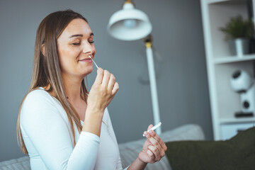 Pregnant woman sitting at a living room of a house with people, introducing a nasal swab in the...