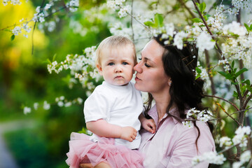 Lovely beautiful feminine mom with her daughter in her arms in spring with cherry blossoms. female natural beauty and beautiful wavy hair. Young European woman in a dress with a baby in a skirt.