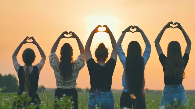 Five girls make a heart shape from their hands at sunset.