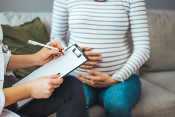 Pregnant Woman Speaks With Her Doctor at a Check-Up. A woman discuses her prenatal health during a routine check up with her obstetrician.