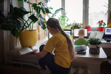 Distant education at home, two siblings doing homework together in one room. Elementary school kids during online class remotely, lockdown, new normal education. Soft focus on girl