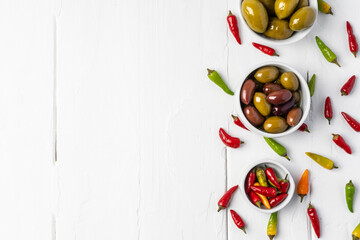 Chili peppers and marinated olives on white wooden background