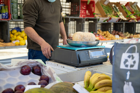 
Street Market Clerk With Mask Weighing Customer's Pumpkin, Assorted Fruits And Vegetables And Recycling Bag