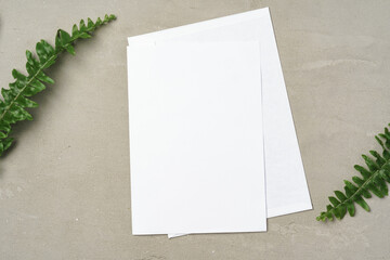 Paper envelope with white blank paper note and plant leaves on table