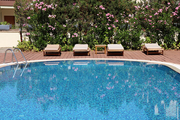 Swimming pool and empty deck chairs are surrounded by oleander flowers. Vacation on summer resort