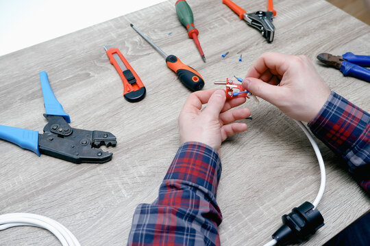 A male electrician changes the plug on an electric wire. Working with electrical tools. Stripper, crimp, screwdriver, wire cutters. Electrician connecting wires