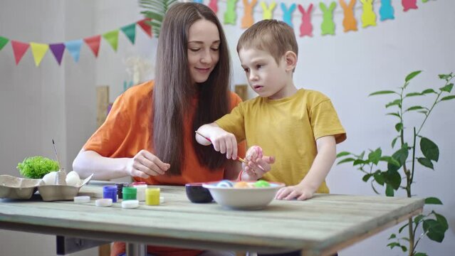 Mom and a son are painting eggs together in a room decorated for the holiday. Concept of preparing the family for Easter, spring mood