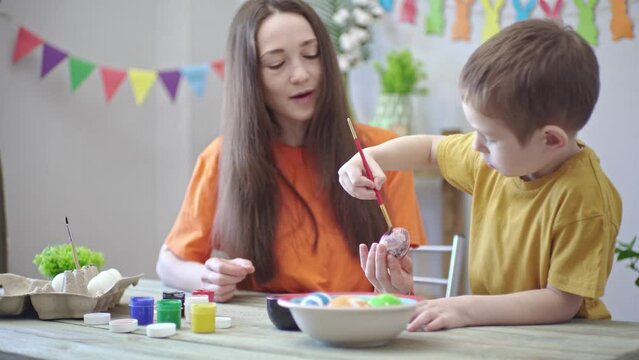 Mom and a son are painting eggs together in a room decorated for the holiday. Concept of family preparation for Easter, festive spring mood