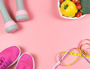 flat lay of pink sneakers, pink dumbbells, measuring tape, and vegatables on pink background with copy space in the middle. frame of . healthy lifestyle background.