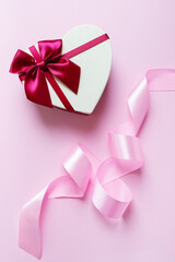 Beautiful festive image with a heart-shaped box and a silk ribbon on a pink background. Vertical view.