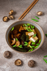 Fototapeta premium Japanese vegan miso soup in a bowl with tofu, shiitake mushrooms, seaweed and green onions. Asian food. Brown grunge background. Side view, selective focus.