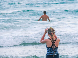 A young girl with a scythe, wearing a scuba mask and a snorkel enters the sea with waves. Diving underwater with a mask and snorkel in the sea. Scuba diving.