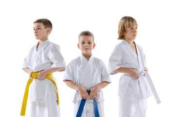 Close-up three sportive kids, little boys, taekwondo or karate athletes in doboks posing isolated on white background. Concept of sport, martial arts
