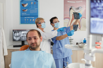 Obraz premium Portrait of patient with toothache waiting for medical expertise during stomatological examination in dentistry office room. In background medical team analyzing teeth radiography. Medicine service