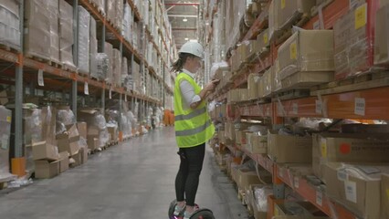 Woman manager or storekeeper works at retail or wholesale warehouse using tablet for inventory control, moving on hoverboard examining at shelves with goods. - Powered by Adobe