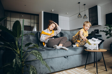 Naklejka premium children at home, sitting on the couch, playing with gadgets