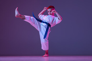 Portrait of sportive kid, male taekwondo, karate athletes in doboks doing basic movements isolated...