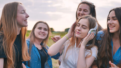 A group of girls of friends are listening to music on headphones and dancing to a friend.