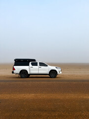 Car at roadside parked in desert. White SUV off road auto vehicle. Morning fog.