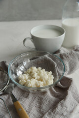 Milk kefir grains in a glass bowl with a cup and a bottle of kefir on white table.