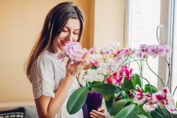 Happy woman smelling blooming purple orchid holding pot. Girl gardener taking care of home plants...