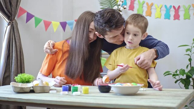 Happy family is coloring Easter eggs in a decorated room. Dad, mom and child preparation for Easter, festive spring mood