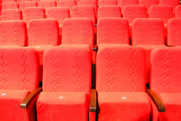 red armchairs. Empty concert hall, theater chairs background ... color photo, empty cinema or concert hall. The red chairs in the cinema hall are illuminated by a light beam. Selective focus