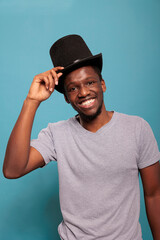 Portrait of male artist with retro top hat on head in front of camera, doing magical performance with artistic prop costume in studio. Person wearing vintage costume topper for fun.