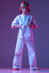 Serious kid, little boy, taekwondo or karate athletes in doboks posing isolated on very peri color background in neon. Concept of sport, martial arts