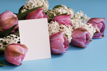 Blank white card and beautiful spring bouquet on a blue background. Greeting card concept. Mock up blank white paper card for text