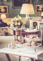 A cake stand full of delicious fancy cakes and sandwiches for an English high tea in a stately home.