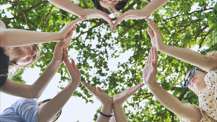 A group of girls makes a heart shape from their hands against the background of tree branches.