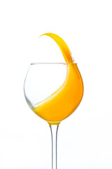 close-up on a transparent wine glass with orange juice splashing in it on a white background