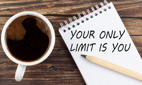 YOUR ONLY LIMIT IS YOU text on notebook with coffee on wooden background