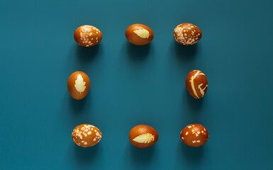 Eggs decorated with organic onion paint and leaves of plants on Easter holiday. Blue background.