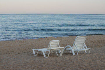 Two sunbeds on a sandy calm beach with turquoise sea water and white sand