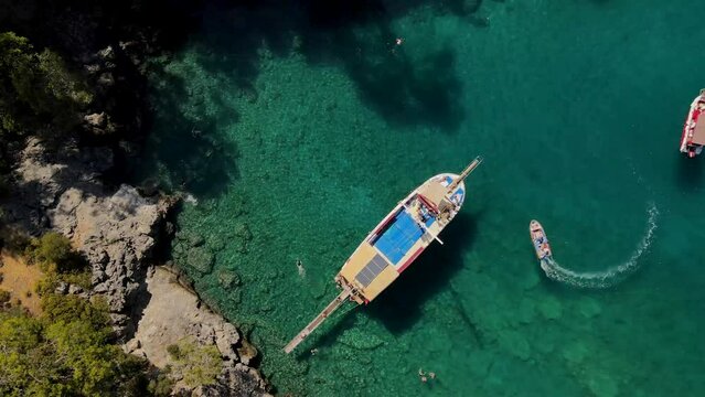 Aerial drone close up view to clear blue sea water with moored boats and yachts. Anchoring in bay in private beach in Turkey travel destination.