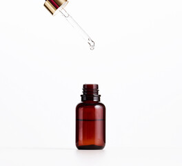 essential oil falling from the amber glass dropper. Blue bottle of cosmetic oil with a pipette, white background