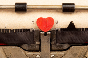 I love you - phrase on typewriter. Valentines Day greetings concept. Little red wooden heart close up. Valentines greeting card.