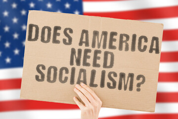 The question " Does America need socialism? " on a banner in men's hand with blurred American flag on the background. Politician. Resistance. Dividing. Conflict. Capitalism. Strike. Society. War. US