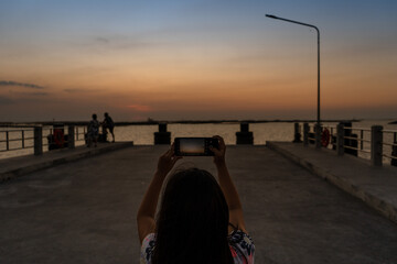 Fototapeta premium Girl take a photo at sunset on the beach