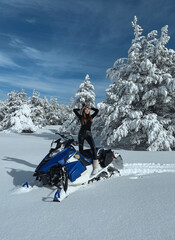 beautiful woman in sportive clothes posing on snowmobile in beautiful snowy nature