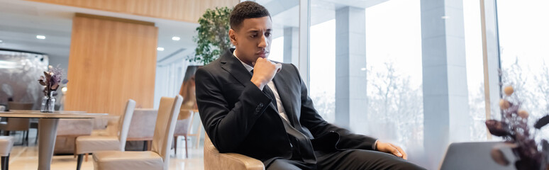 serious and pensive african american security man sitting in hotel lounge, banner.