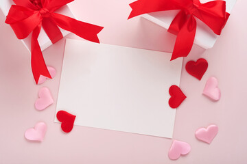White gift boxes with red ribbon and small red decorative hearts on pink background. Top view with...