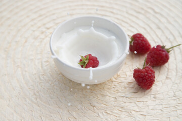 Raspberry berry flies into a plate of milk with splashes.