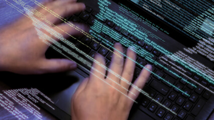 Programmer at work - Caucasian man hands typing on laptop keyboard, elements of software code...