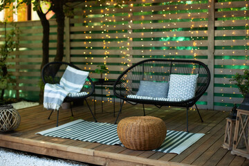 Modern lounge outdoors in backyard. Terrace house with wooden floor, comfortable sofa, armchair and wicker ottoman. Cozy space in patio or balcony for relax. Wooden veranda with garden furniture.	
 - obrazy, fototapety, plakaty