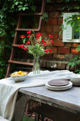 A bouquet of red poppies in a glass vase. Flowers in a vase at home. Interior Terrace, patio. Wooden table and plates for garden party or dinner. Table for lunch outside in garden in yard of house.	
