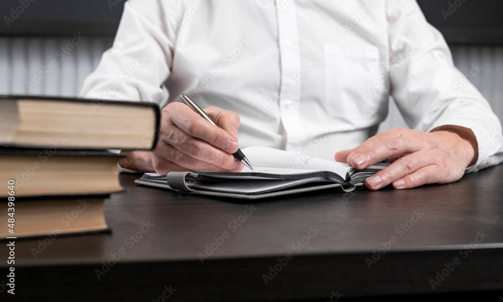 Poster man sitting at office desk with books or codes and taking notes in diary. man hands closeup. plannin