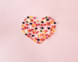 A heart of colorful candies on a pink background. Minimal Valentine's Day concept